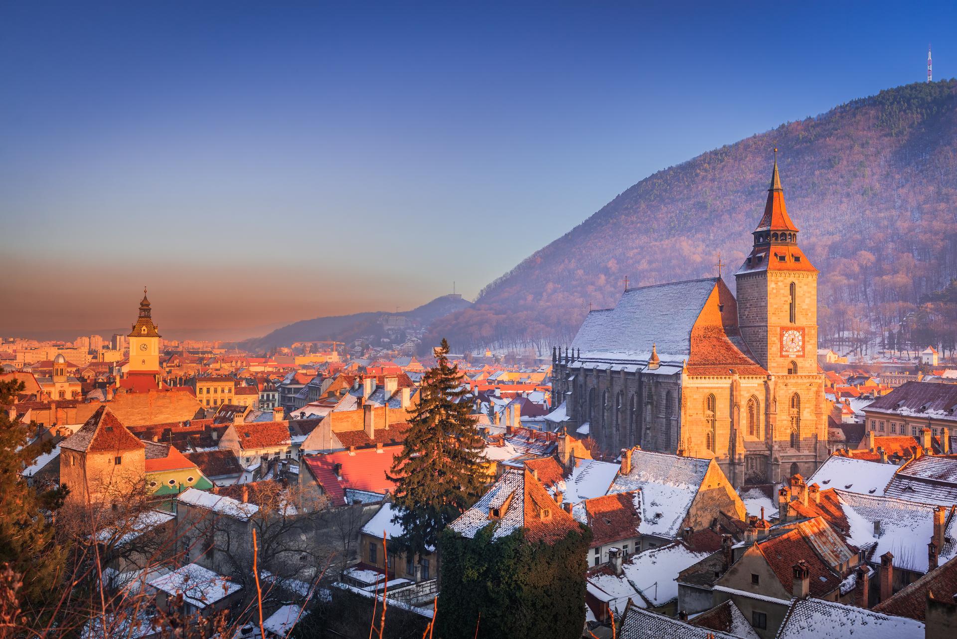 Brasov, Romania. Winter snowy downtown, sunset time, Black Church and Carpathian Mountains